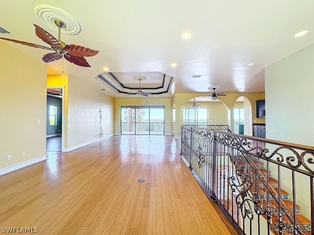 hallway with a tray ceiling and light wood-type flooring