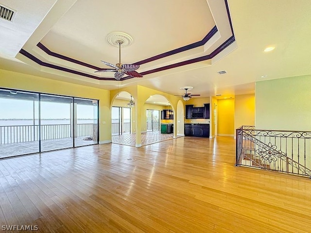 unfurnished living room with light hardwood / wood-style floors, ceiling fan, and a raised ceiling