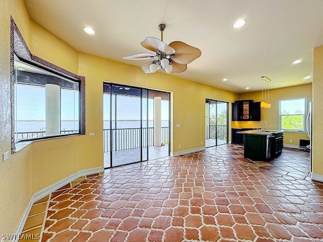 kitchen featuring ceiling fan, dark tile flooring, an island with sink, sink, and pendant lighting