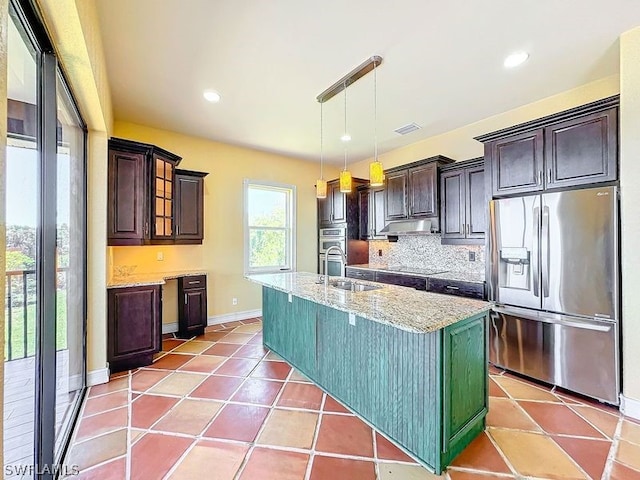 kitchen with light stone counters, hanging light fixtures, appliances with stainless steel finishes, sink, and a center island with sink