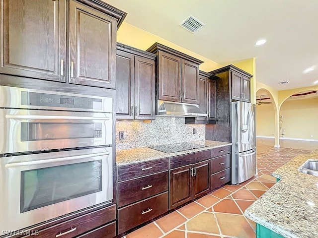 kitchen with dark brown cabinetry, appliances with stainless steel finishes, tasteful backsplash, and light tile floors