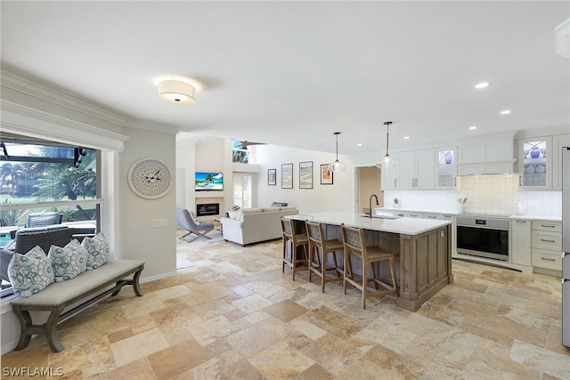 kitchen featuring decorative light fixtures, backsplash, a center island with sink, oven, and sink