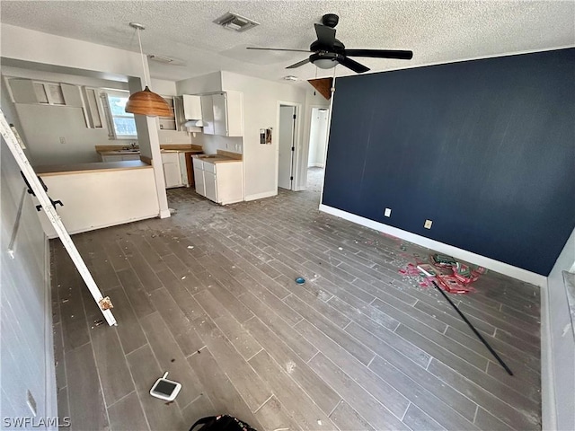 unfurnished living room featuring dark hardwood / wood-style floors, ceiling fan, and a textured ceiling