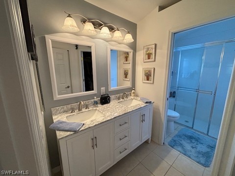 bathroom featuring dual bowl vanity, toilet, tile floors, and a shower with door