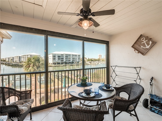 sunroom with ceiling fan and a water view