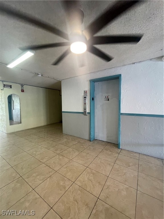 tiled empty room with ceiling fan and a textured ceiling