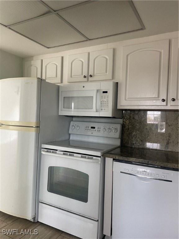 kitchen with white appliances, white cabinetry, dark stone counters, dark hardwood / wood-style flooring, and decorative backsplash