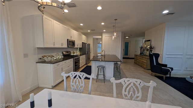 kitchen with an island with sink, white cabinetry, a kitchen bar, hanging light fixtures, and appliances with stainless steel finishes