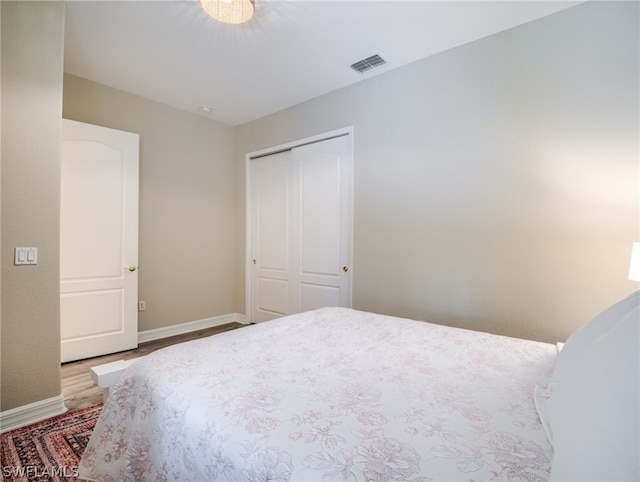 bedroom with a closet, visible vents, baseboards, and wood finished floors