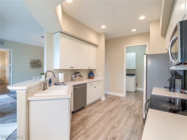 kitchen with stainless steel appliances, washer / clothes dryer, white cabinetry, a sink, and light wood-type flooring