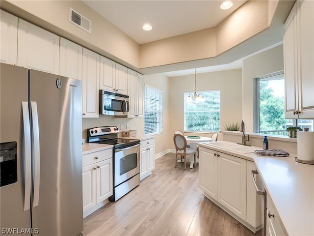 kitchen with stainless steel appliances, an inviting chandelier, light wood-type flooring, and white cabinetry