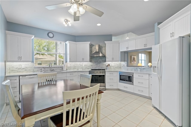 kitchen featuring ceiling fan, wall chimney range hood, backsplash, white cabinetry, and stainless steel appliances