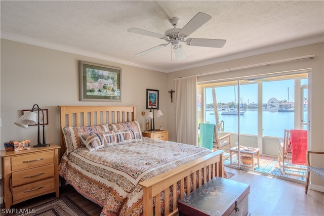 bedroom featuring a water view, ceiling fan, a textured ceiling, hardwood / wood-style floors, and ornamental molding