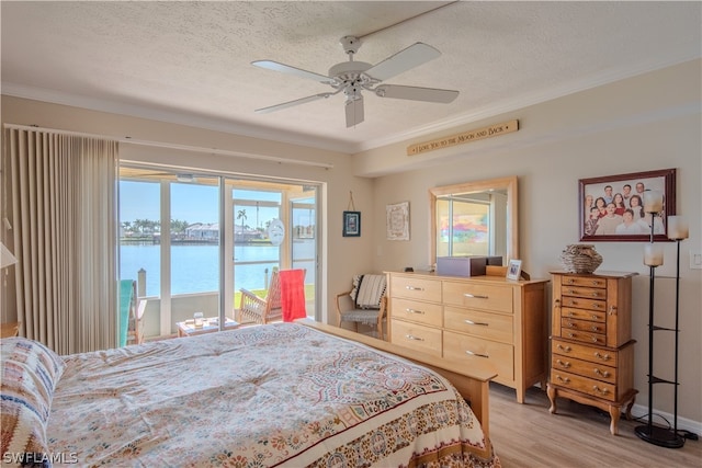 bedroom featuring access to outside, hardwood / wood-style floors, a water view, ceiling fan, and a textured ceiling