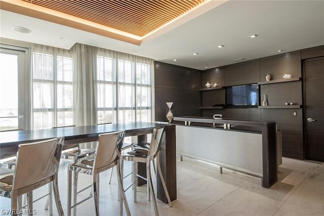 kitchen with dark brown cabinetry, light tile floors, a breakfast bar, stainless steel counters, and a tray ceiling