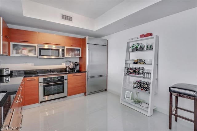 kitchen featuring light tile floors, a kitchen bar, a tray ceiling, dark stone counters, and stainless steel appliances