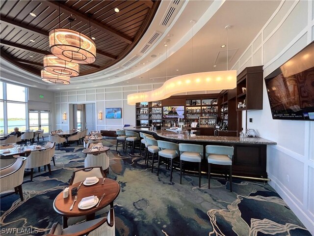 bar with dark brown cabinetry, a towering ceiling, a raised ceiling, and stone counters