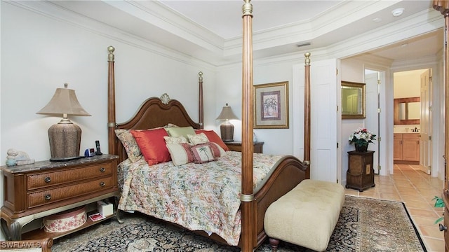 bedroom featuring light tile patterned floors, a tray ceiling, ornamental molding, and ensuite bathroom