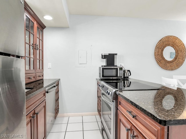 kitchen with appliances with stainless steel finishes, dark stone countertops, and light tile floors