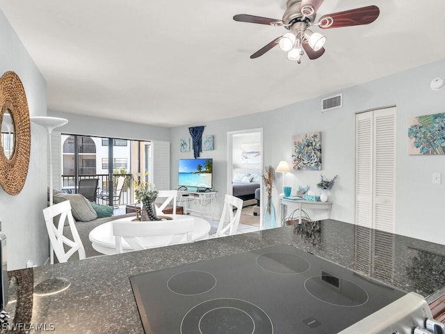 kitchen featuring ceiling fan, dark stone countertops, and cooktop