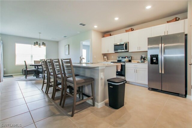 kitchen featuring decorative light fixtures, stainless steel appliances, white cabinets, and a center island with sink