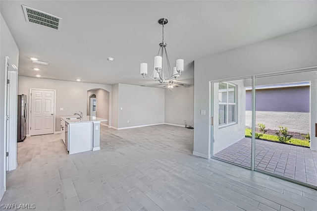 interior space featuring stainless steel fridge, light hardwood / wood-style floors, a center island with sink, decorative light fixtures, and a chandelier