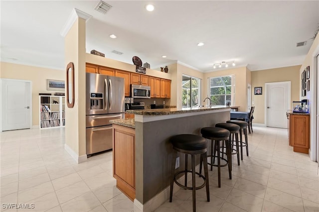 kitchen with stainless steel appliances, a kitchen breakfast bar, an island with sink, dark stone counters, and light tile patterned flooring