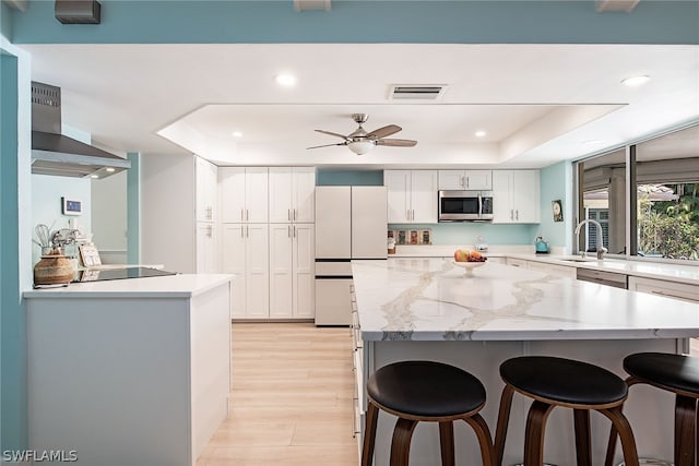 kitchen featuring wall chimney exhaust hood, a kitchen island, white cabinets, light wood-type flooring, and stainless steel appliances