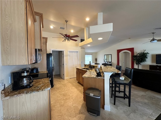 kitchen with ceiling fan, an island with sink, and light stone countertops