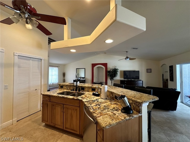 kitchen featuring a kitchen island with sink, a breakfast bar, sink, light stone counters, and ceiling fan