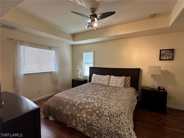 bedroom with dark hardwood / wood-style flooring, ceiling fan, and a raised ceiling