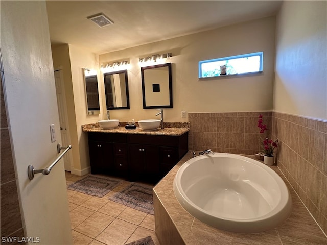 bathroom featuring dual sinks, vanity with extensive cabinet space, tile floors, and tiled bath