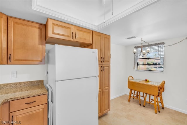 kitchen with light stone counters, white refrigerator, decorative light fixtures, a notable chandelier, and light brown cabinetry