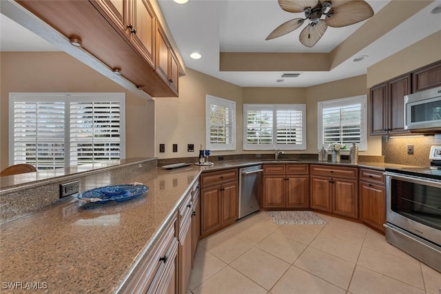 kitchen featuring a tray ceiling, light tile patterned flooring, dark stone counters, and stainless steel appliances