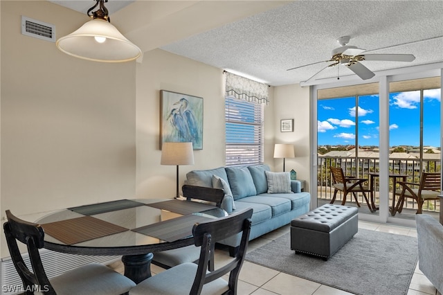 tiled living room featuring ceiling fan, a wall of windows, and a textured ceiling