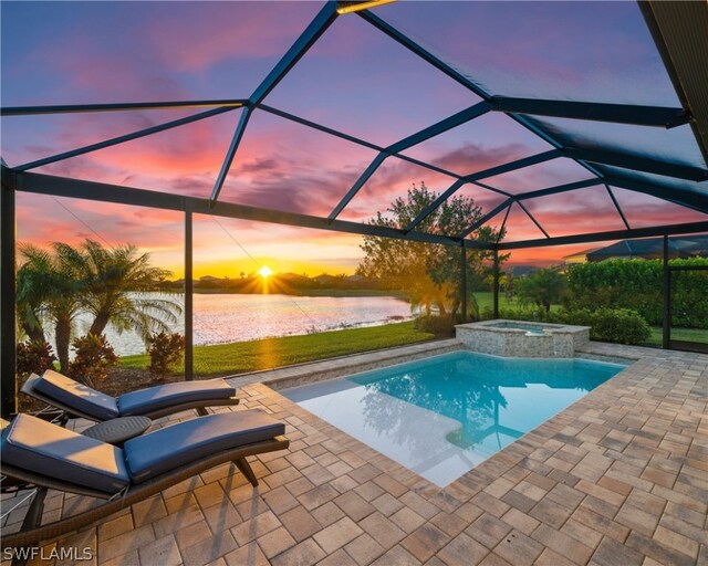 pool at dusk featuring a water view, glass enclosure, an in ground hot tub, and a patio area