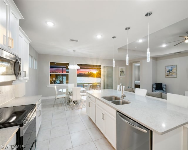 kitchen with a kitchen island with sink, stainless steel appliances, a sink, white cabinets, and decorative light fixtures