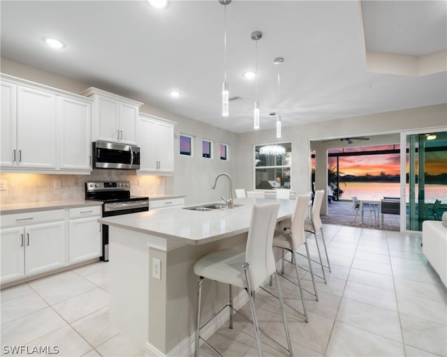 kitchen with pendant lighting, a center island with sink, stainless steel appliances, white cabinets, and a sink