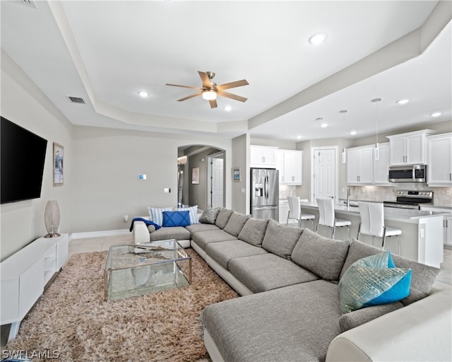 living room featuring visible vents, a raised ceiling, arched walkways, a ceiling fan, and recessed lighting