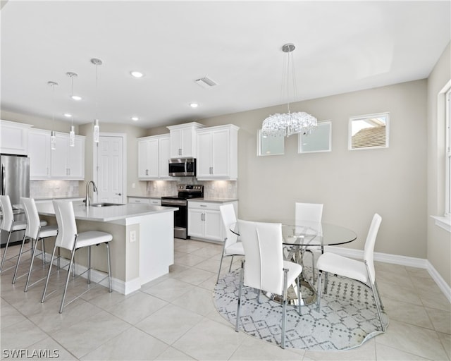 kitchen with appliances with stainless steel finishes, hanging light fixtures, light countertops, white cabinetry, and a sink