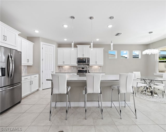 kitchen featuring appliances with stainless steel finishes, hanging light fixtures, a kitchen island with sink, light countertops, and a sink