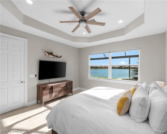 bedroom with light wood-style floors, a raised ceiling, and baseboards