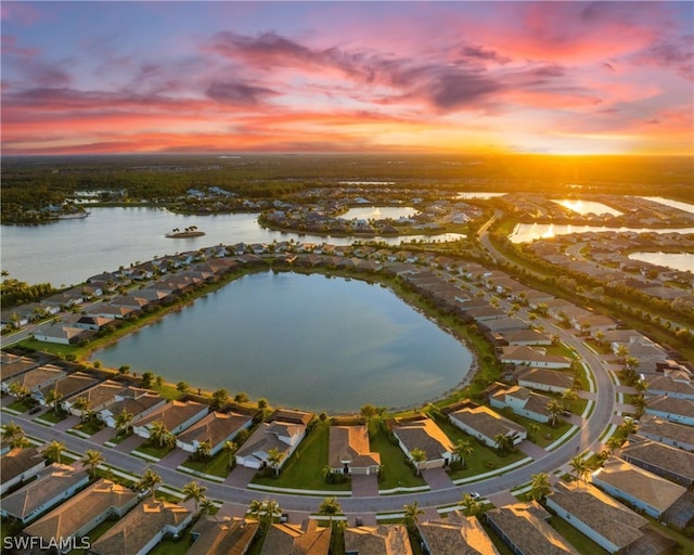 aerial view at dusk with a water view and a residential view