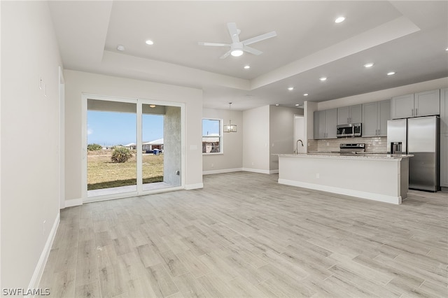 unfurnished living room with ceiling fan with notable chandelier, a tray ceiling, light hardwood / wood-style flooring, and sink