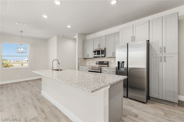 kitchen with a kitchen island with sink, pendant lighting, stainless steel appliances, and light stone counters