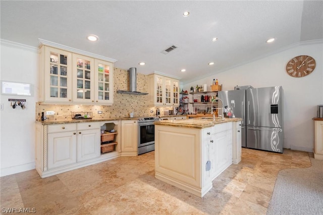 kitchen featuring wall chimney exhaust hood, ornamental molding, an island with sink, appliances with stainless steel finishes, and light stone counters