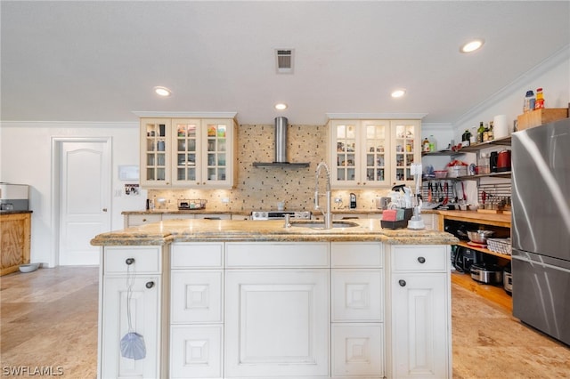 kitchen with a kitchen island with sink, white cabinets, wall chimney exhaust hood, stainless steel fridge, and light stone countertops