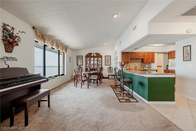 kitchen with kitchen peninsula, vaulted ceiling, oven, light stone counters, and light tile floors