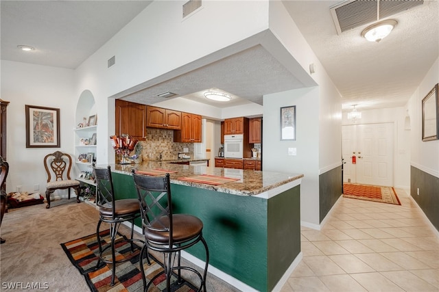 kitchen with kitchen peninsula, backsplash, oven, light stone counters, and light tile floors