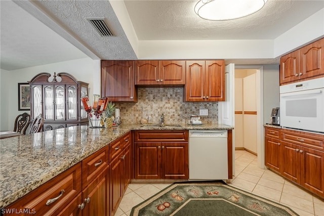 kitchen with sink, white appliances, light tile floors, and light stone countertops